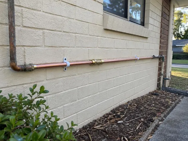 Repaired copper water pipe running along an exterior brick wall near a window in Highfields
