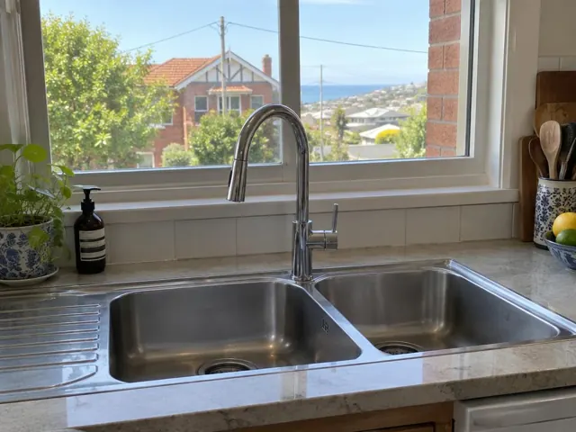 Chrome kitchen mixer tap over a double sink with window and tiled splashback in Merewether