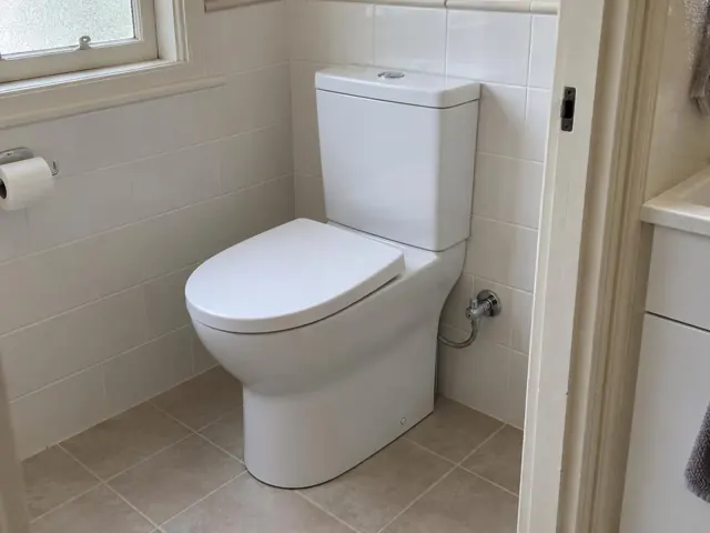 White close-coupled toilet in a tiled bathroom beside a window and vanity in Merewether